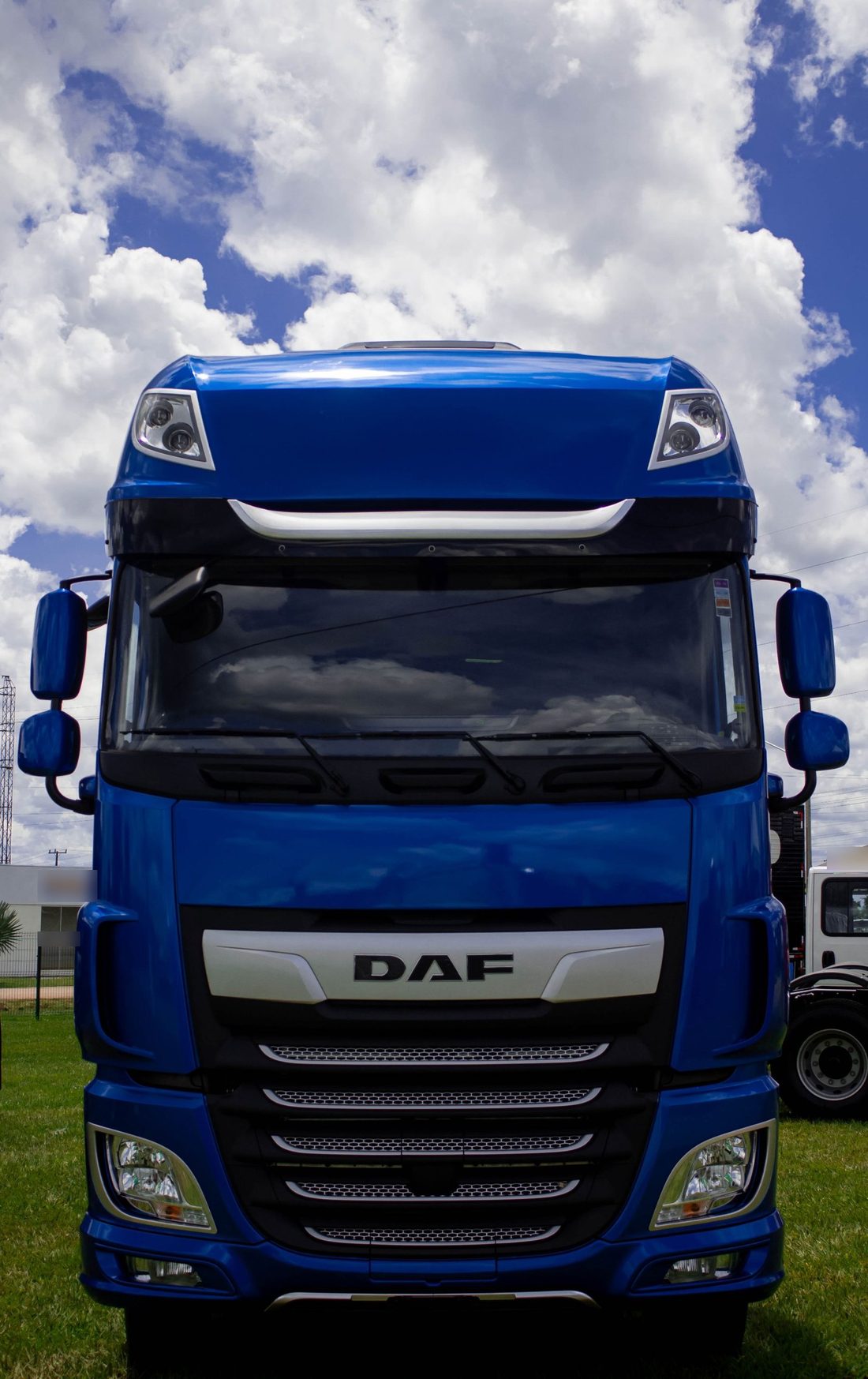 Front of a blue lorry cab parked on grass under a bright, cloudy sky